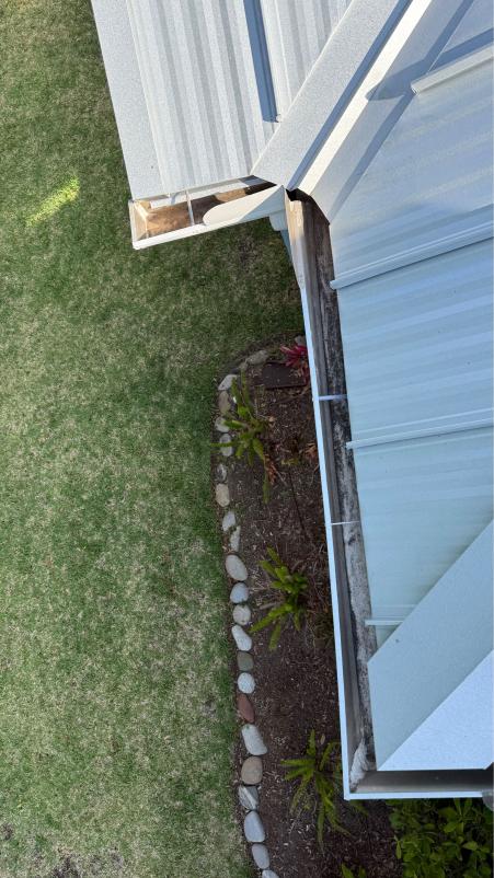 roof edge and gutters with water drainage visible on a green lawn and garden bed along the side