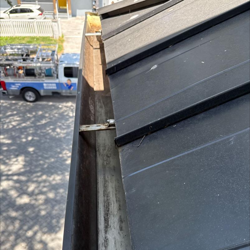 gutter cleaning service showing a dirty gutter with accumulated debris and a truck in the background
