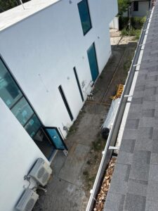 gutter cleaning and window washing on a modern building with visible air conditioning units and construction materials in the area