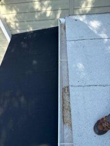 roof inspection showing black and white roofing materials with a foot in work boots on the edge of the roof