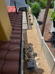 gutter cleaning along a tile roof with a view of the backyard and flower pots on a pebbled pathway