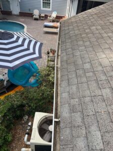 gutter cleaning service being performed on a residential roof with pool and patio area visible in background
