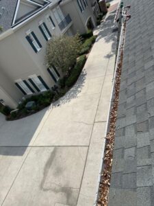 gutter cleaning with debris accumulation visible along the edge of the roof and clean pavement in the driveway