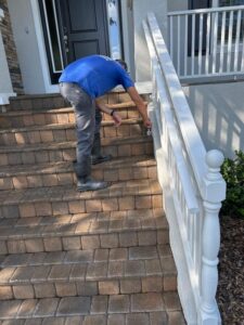 man inspecting or cleaning the railing on a brick paver staircase near a house entrance in south tampa