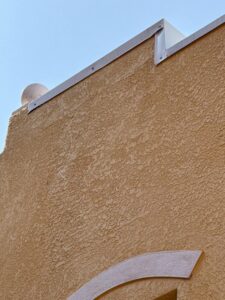 yellow textured wall with white trim and a round feature at the top against a clear blue sky