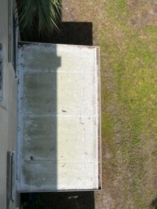 cleaning a flat roof with visible debris and dirt on the surface near grass and a nearby palm tree