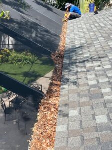 gutter cleaning service removing debris from gutters on a sloped roof near a well-maintained garden and patio furniture