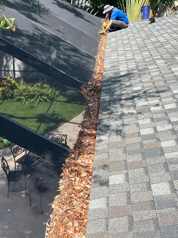 gutter cleaning service removing debris from gutters on a sloped roof near a well-maintained garden and patio furniture