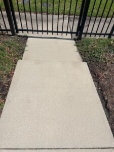 clean concrete sidewalk leading to a black gate with grass and dirt on the sides