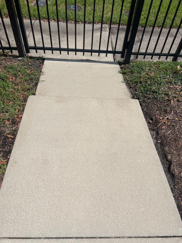 clean concrete sidewalk leading to a black gate with grass and dirt on the sides