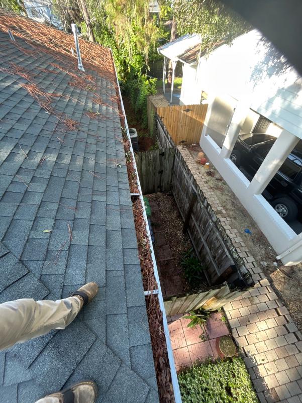 gutter cleaning service removing debris from a residential roof with a clear view of the surrounding yard and fence
