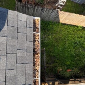 gutter cleaning service clearing debris from a gutter filled with leaves near a roof edge and green backyard visible