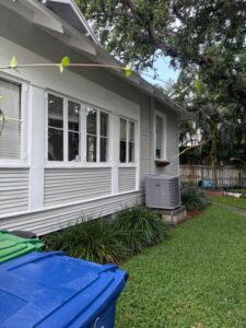 gutter cleaning services being performed on a house with a grey exterior and visible air conditioning unit