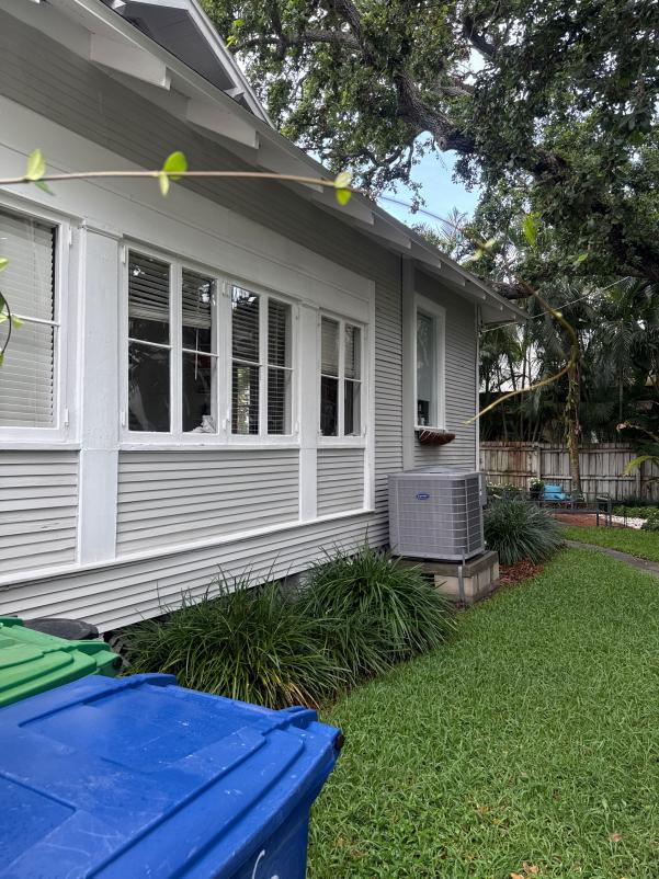 gutter cleaning services being performed on a house with a grey exterior and visible air conditioning unit
