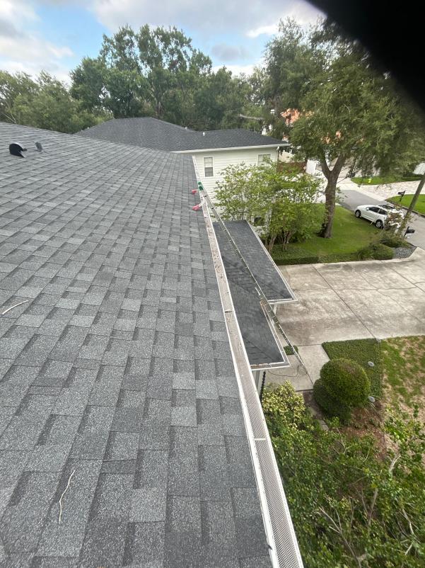 gutter cleaning service being performed on a house with a shingle roof and greenery around the property