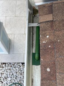 gutter cleaning service with a green gutter guard installed on a roof edge near a stone patio area