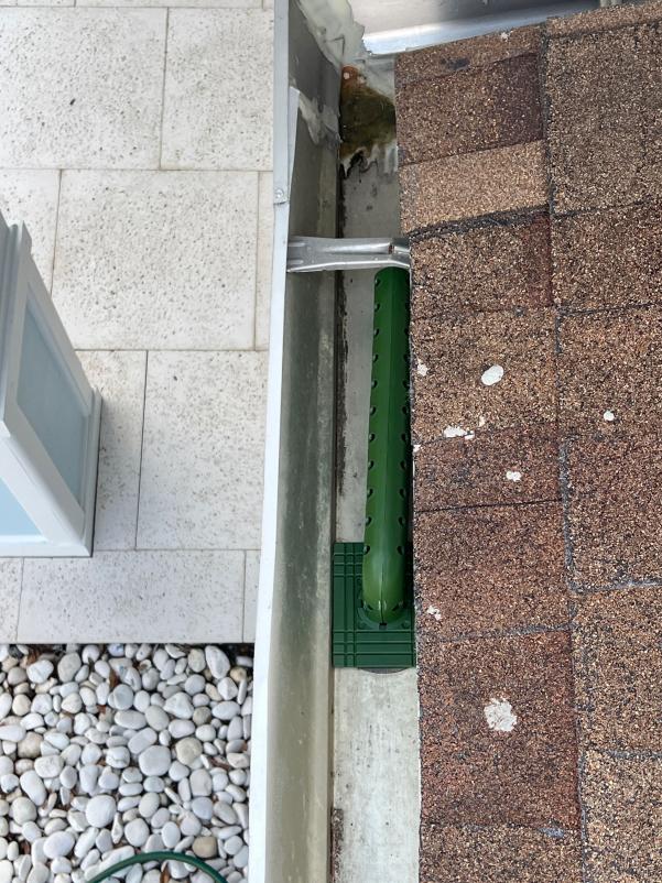 gutter cleaning service with a green gutter guard installed on a roof edge near a stone patio area