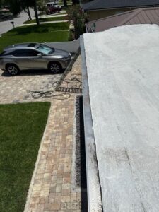 gutter cleaning services being performed with a ladder positioned on a driveway next to a parked vehicle and landscaped lawn