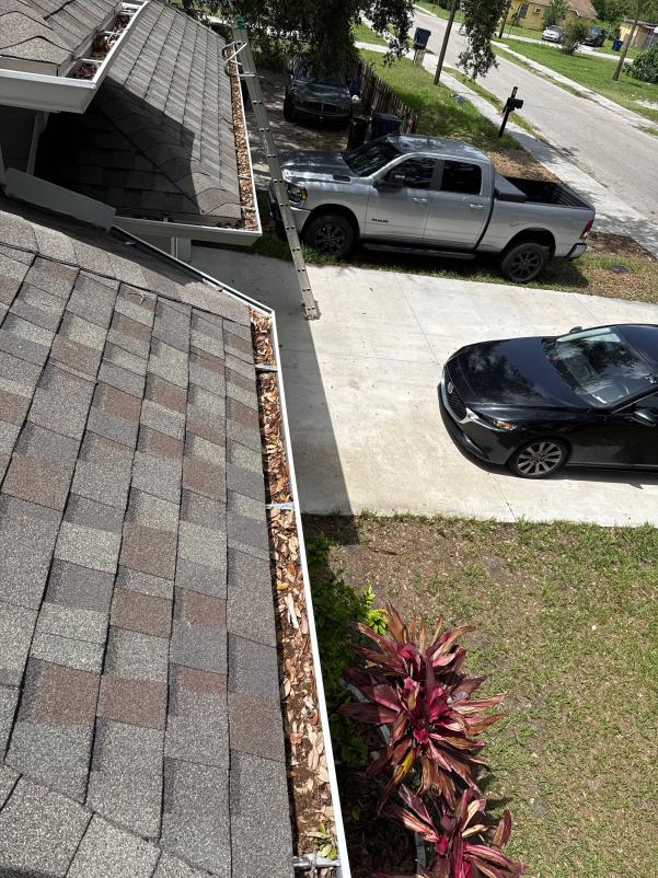 gutter cleaning service with debris buildup visible along roofline near parked vehicles and surrounding landscaping