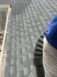 roof cleaning in progress with a view of shingles and a person holding equipment on a sloped surface