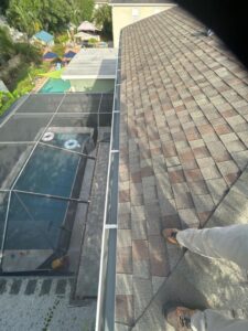 person walking on a roof near a gutter system overlooking a pool area in a residential backyard