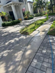 pressure washing of a concrete driveway with hoses laid out on the ground and clean areas visible