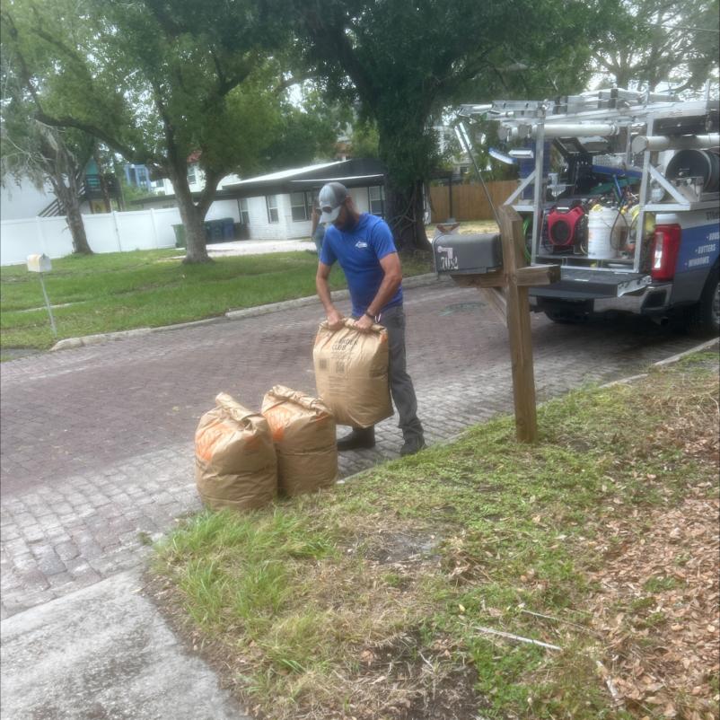 a worker lifting bags likely containing debris or leaves with a service vehicle parked nearby on a residential street