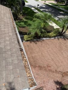 gutter cleaning showing leaves and debris along the edge of a roof with a brick driveway and landscaping visible