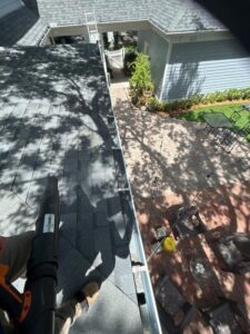 gutter cleaning in progress using a leaf blower on a sloped roof with a view of paver patio and furniture