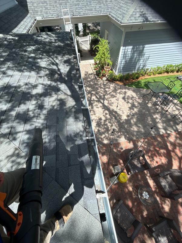 gutter cleaning in progress using a leaf blower on a sloped roof with a view of paver patio and furniture
