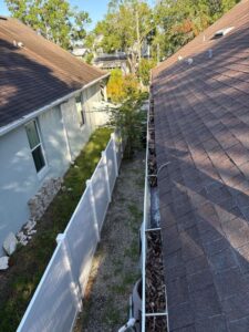gutter cleaning service showing debris buildup on roof edges near a narrow side yard with a white fence