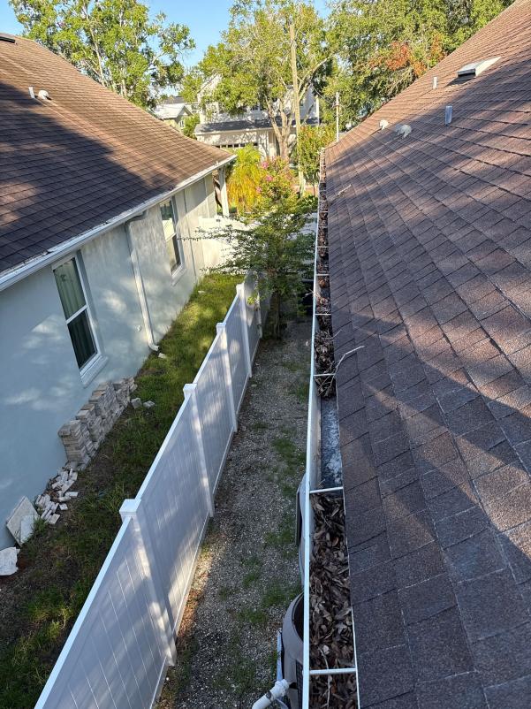 gutter cleaning service showing debris buildup on roof edges near a narrow side yard with a white fence