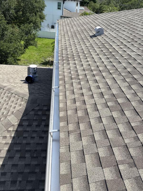 gutter installation on a sloped roof with shingles and visible plumbing vent pipes and gutters along the edge