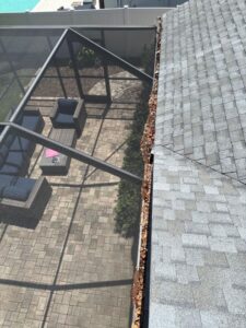 gutter cleaning with debris accumulated on roof edge near a screened patio area with outdoor furniture visible below