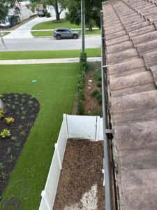 cleaning and inspecting gutters with a view of landscaped yard and fence from rooftop perspective