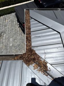 gutter cleaning service retrieving debris like leaves and twigs from a metal roof area near a drainage system