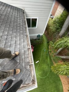 cleaning gutters on a roof with visible debris using safety gear and equipment nearby