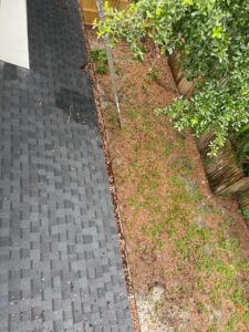gutter cleaning with debris on the roof and ground near a ladder and trees in a residential area