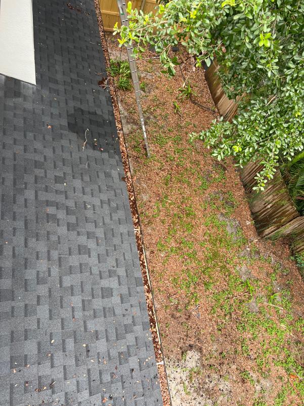 gutter cleaning with debris on the roof and ground near a ladder and trees in a residential area