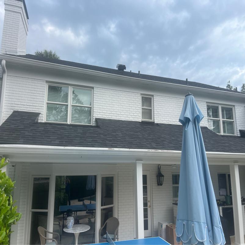 gutter cleaning in progress on a two-story white house with dark shingles and a patio umbrella in view