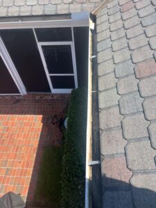 gutter cleaning service showing a clear view of roof shingles and brick patio with green bushes near the gutter