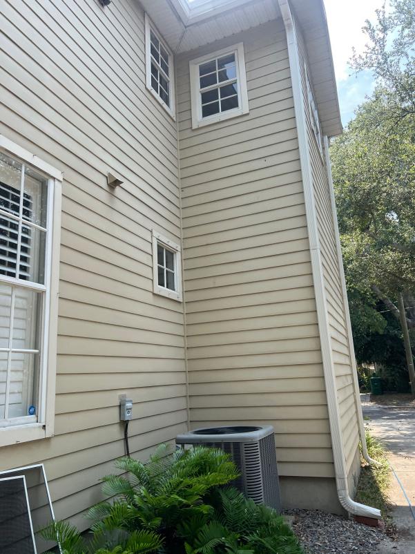 house washing on tan vinyl siding with multiple windows and landscaping visible near an air conditioning unit