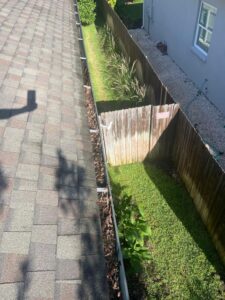 gutter cleaning service showing cleared debris from gutters along a roofline with adjacent greenery and fencing visible