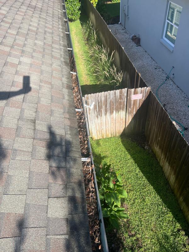 gutter cleaning service showing cleared debris from gutters along a roofline with adjacent greenery and fencing visible