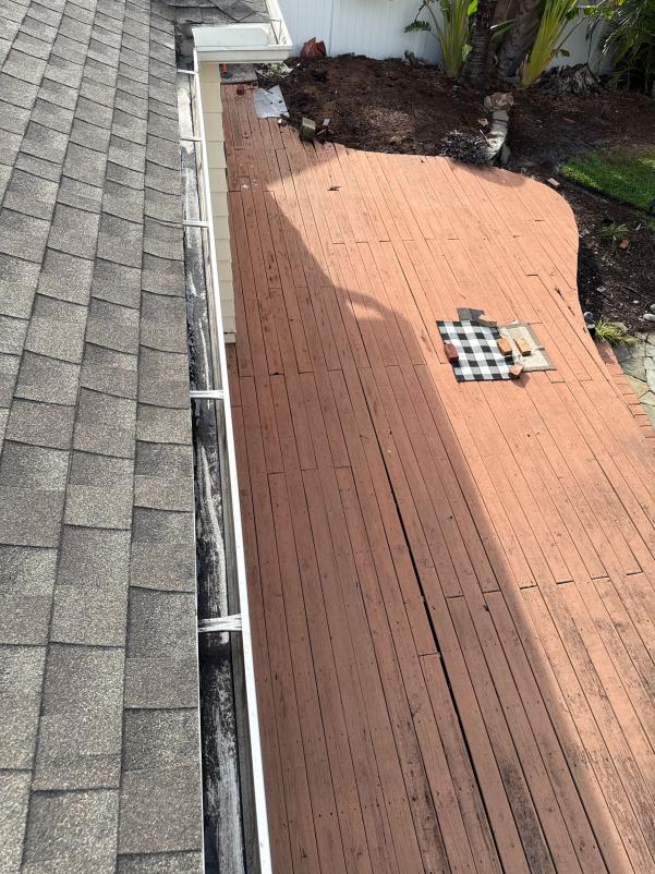 gutter cleaning service with a view of a wooden deck and roof shingles visible from above