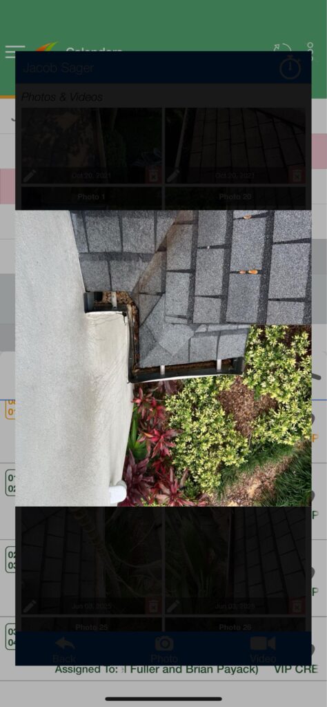 gutter cleaning with visible debris and leaf buildup near roof edge against grey shingles and landscaped greenery below