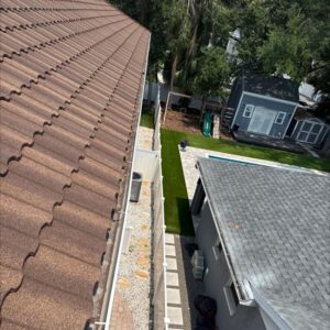 gutter cleaning service being performed on a sloped roof with a clear view of a manicured lawn and pool area