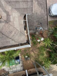 gutter cleaning near a roof showing debris and a landscaped area with palm trees and a parked car below
