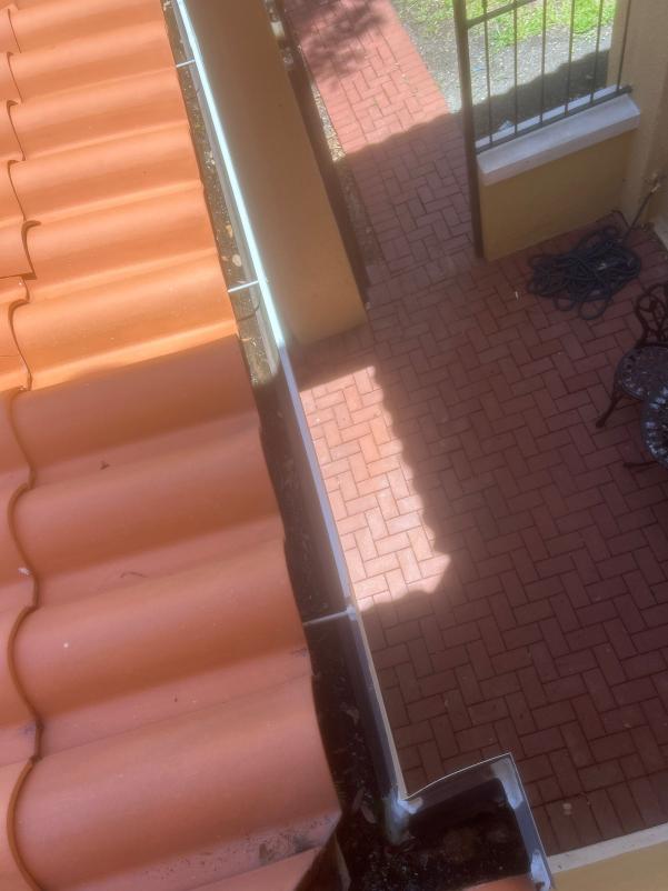 gutter cleaning along a tiled roof with a clear view of a brick patio below