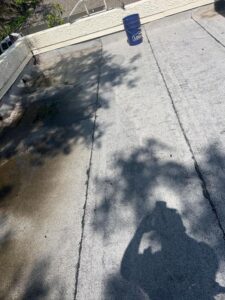 roof cleaning in progress with a light colored surface and a blue bucket nearby on flat roofing area